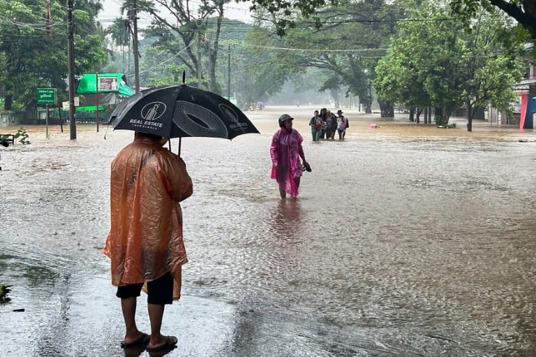 Varias personas caminan por una calle anegada a causa de las abundantes lluvias en Myitkyina, el 2 de julio de 2024 al norte de Birmania (.)