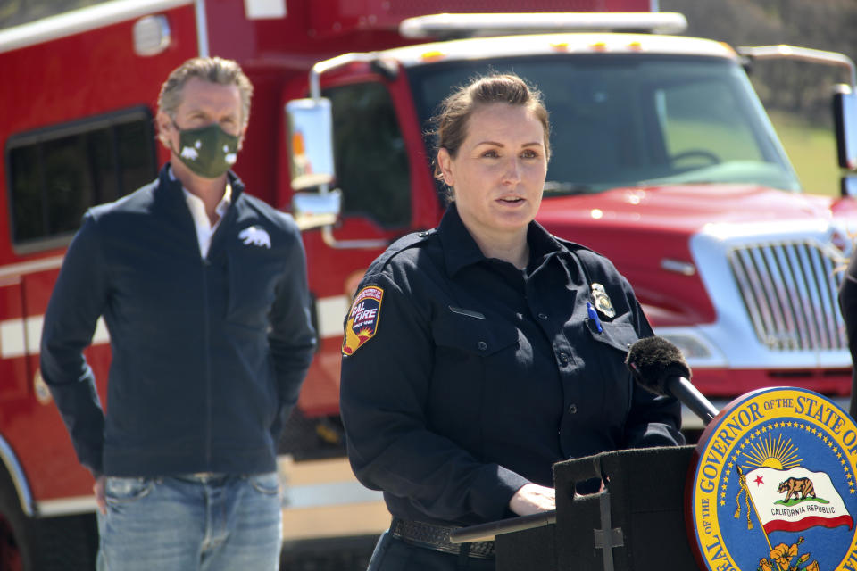 Beth Bowersox, a communications operator at the California Department of Forestry and Fire Protection, speaks to reporters during a news conference as California Gov. Gavin Newsom listens in the background on Tuesday, April 13, 2021, at the Loafer Creek State Recreation Area in Oroville, California. Newsom on Tuesday signed a law authorizing more than half a billion dollars in new spending to prepare for wildfire season. (AP Photo/Adam Beam)