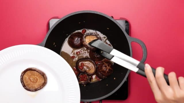 Removing mushrooms and goji berries from the pot with tongs