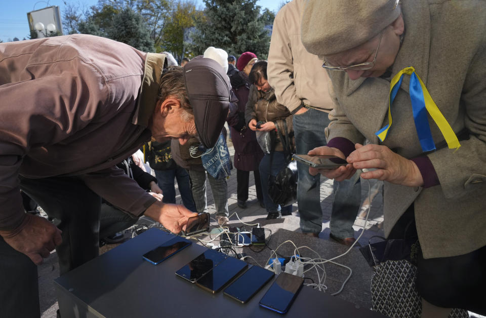 People charge their phones, try to connect to the internet and make phone calls, in central square in Kherson, Ukraine, Tuesday, Nov. 15, 2022. Waves of Russian airstrikes rocked Ukraine on Tuesday, with authorities immediately announcing emergency blackouts after attacks from east to west on energy and other facilities knocked out power and, in the capital, struck residential buildings. (AP Photo/Efrem Lukatsky)