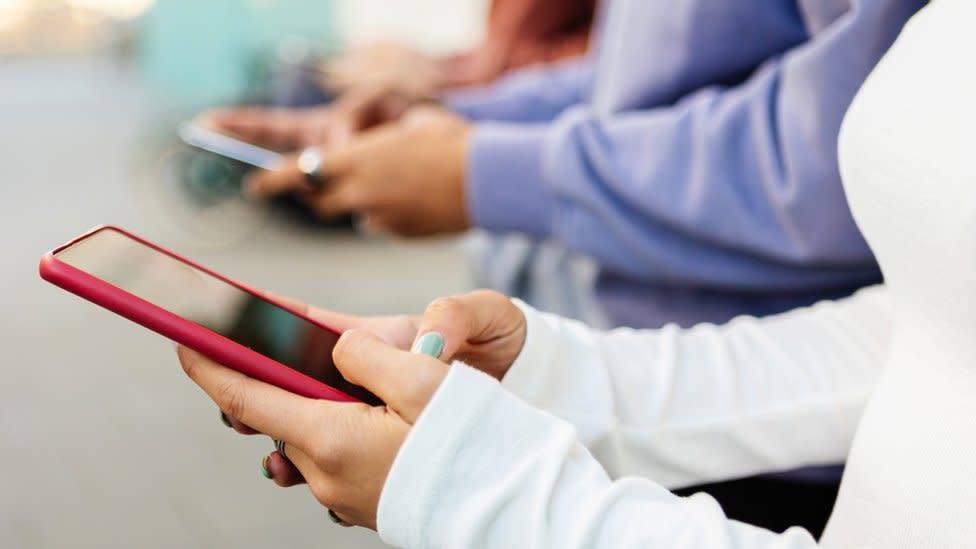 Close up view of the hands of a group of teenagers as they hold their mobile phones