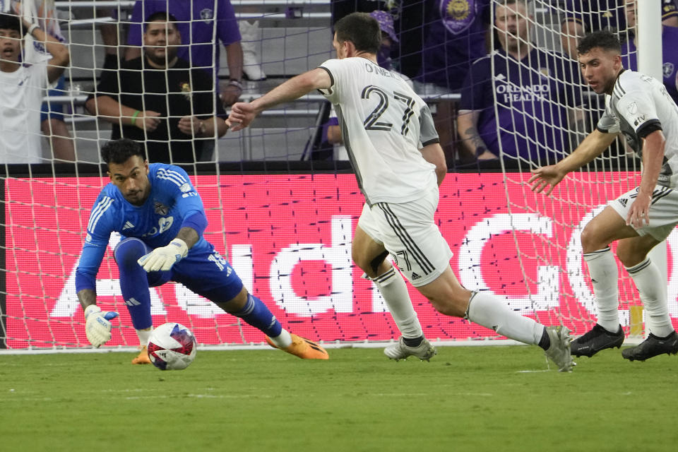 Toronto FC goalkeeper Greg Ranjitsingh, left, blocks a shot by Orlando City as teammates Shane O'Neill (27) and Kobe Franklin, right, come in to assist during the first half of an MLS soccer match Tuesday, July 4, 2023, in Orlando, Fla. (AP Photo/John Raoux)