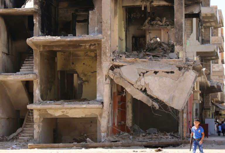 A Syrian boy carries a toy gun past a destroyed building in the northeastern Syrian city of Qamishli