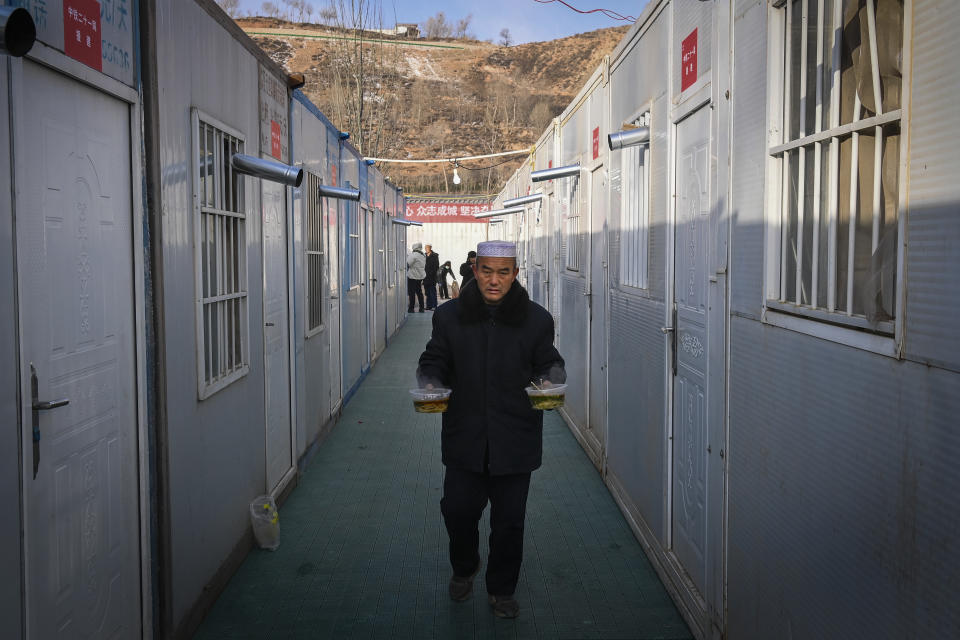 In this photo released by Xinhua News Agency, a man holding bowls of hot beef noodles walks through the temporary plank house set up after the earthquake in Meipo Village, Jishishan County of northwest China's Gansu Province, Thursday, Dec. 21, 2023. The strong earthquake that hit northwest China and killed at least 148 people, has caused tens of millions of estimated economic losses in the agricultural and fisheries industries, state media reported Saturday, Dec. 23, 2023. (Fan Peishen/Xinhua via AP)