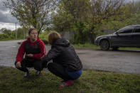 Two Ukrainian villagers squat during Russian shelling in a town north Derhachi, east Ukraine, Sunday, May 15, 2022. (AP Photo/Bernat Armangue)