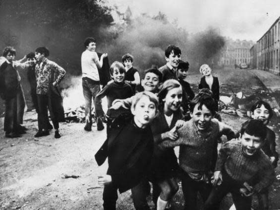 A group of children playing up to the camera while a fire smoulders in the street in Belfast, 1971 (Getty)