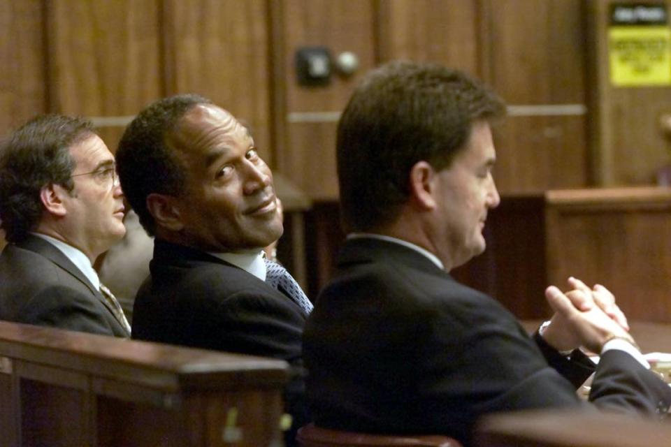 O.J. Simpson, en el centro, mira hacia atrás a algunos estudiantes en la sala del tribunal mientras está sentado con sus abogados Yale Galanter, a la derecha, y Lee Cohn, a la izquierda, en el tribunal de circuito de Miami, el miércoles 10 de octubre de 2001, en Miami.