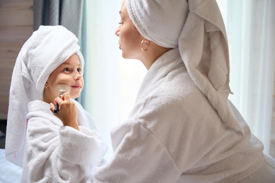 Mother watching her little daughter applying blush on her cheek, first make-up, girls having fun and resting, spa day