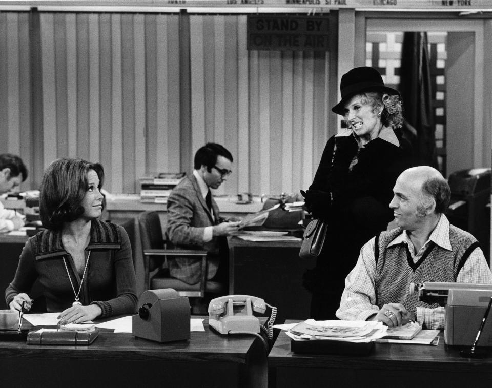 Mary Tyler Moore and Gavin MacLeod sit at a desk while Cloris Leachman stands behind them