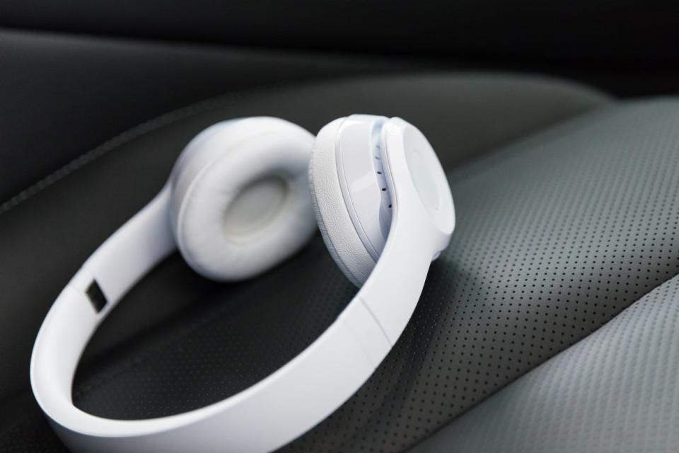 White wireless headphones on a black leather car seat.