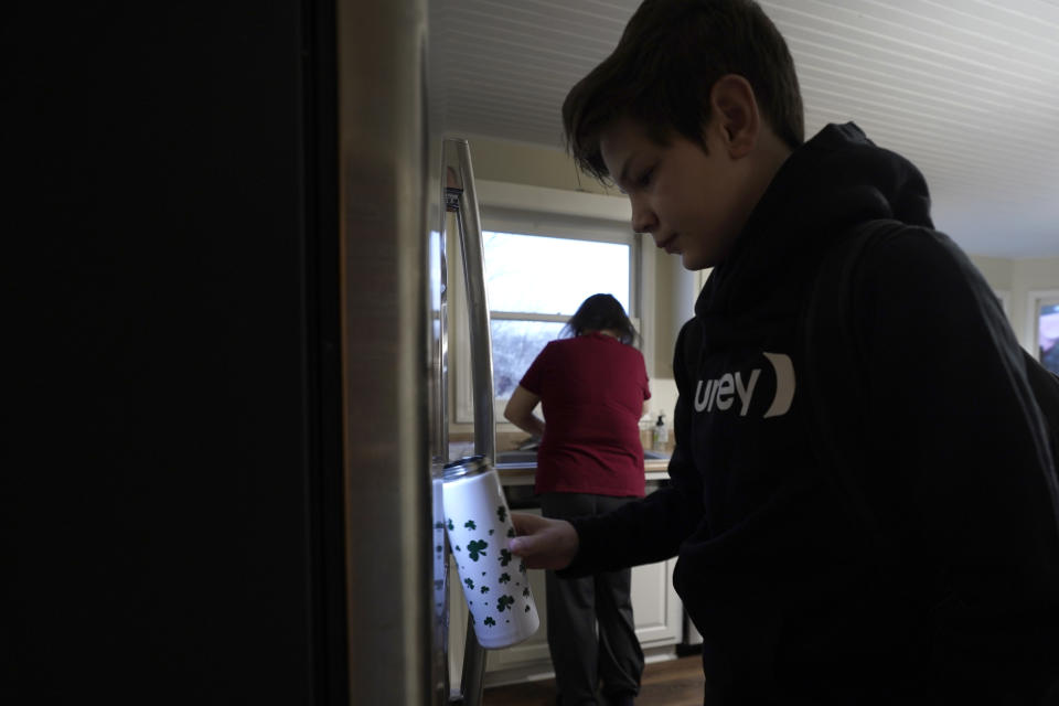 Kari Wegg, background, continues making breakfast as her youngest son, Gunnar, gets water from the refrigerator before catching a bus for school in their Westfield, Ind., home on Tuesday, March 23, 2021. (AP Photo/Charles Rex Arbogast)