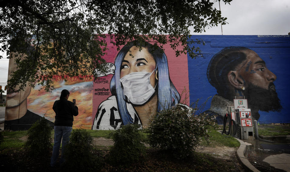 A woman photographs a mural of Cardi B that was updated by the artist Colton Valentine to include a face mask during the coronavirus outbreak in San Antonio, Monday, March 30, 2020. (AP Photo/Eric Gay)