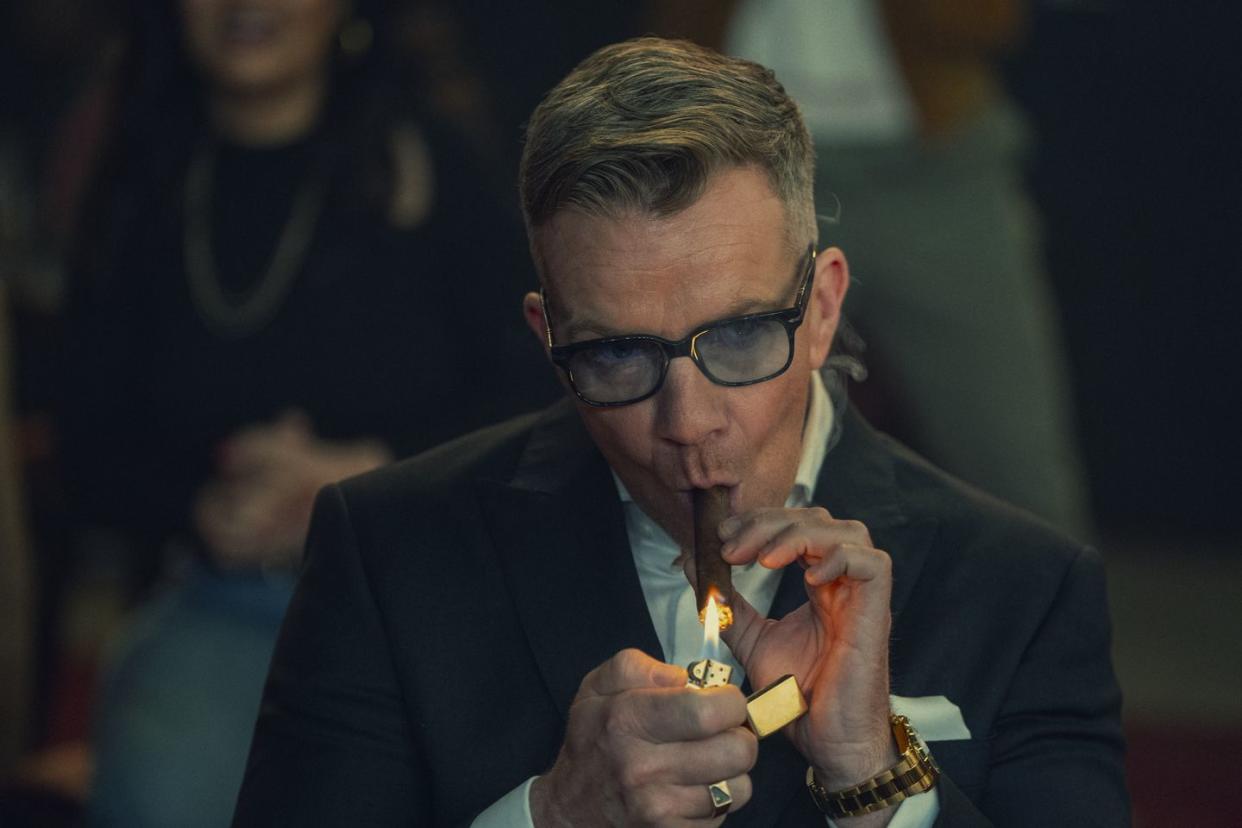 max beesley in the gentlemen, a man in a suit lights a cigar