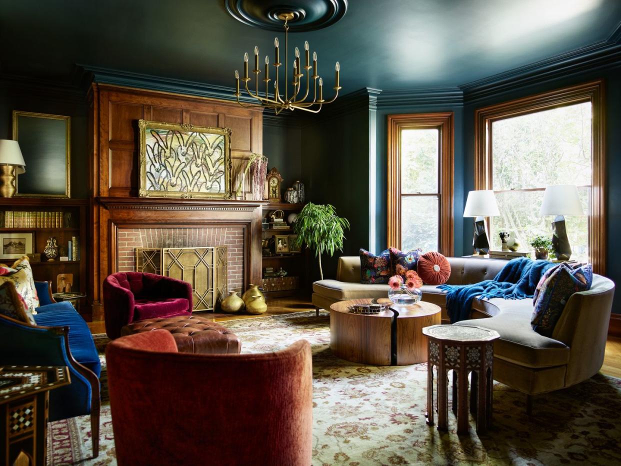 living room to complement the restored wood accents in this boston colonial revival, local designer cecilia casagrande settled on a deep, rich paint farrow ball hague blue chandelier arteriors sofa jonathan adler pillow fabrics from left pierre frey, house of hackney, romo painting hunt slonem swivel armchairs thayer coggin coffee table and side table vintage, autrefois antiques ottoman cisco brothers rug ramble market table lamps kelly wearstler for circa lighting