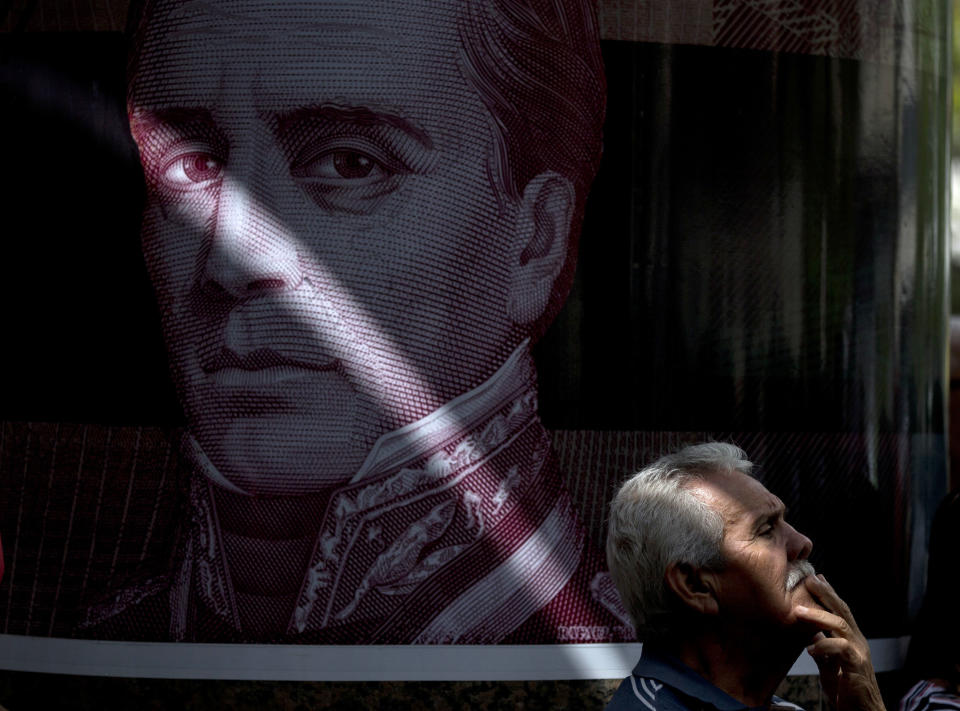 In this Sept. 6, 2018 photo, a retired man stands next to a poster of Venezuelan hero Rafael Urdaneta, during an anti-government protest, in Caracas, Venezuela. Demonstrators gathered near the Central Bank demanding full payment of their pensions. (AP Photo/Fernando Llano)