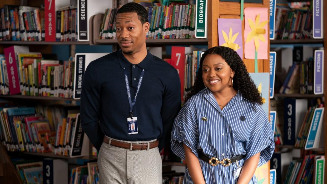  Gregory and Janine standing next to each other smiling in the library on Abbott Elementary. 