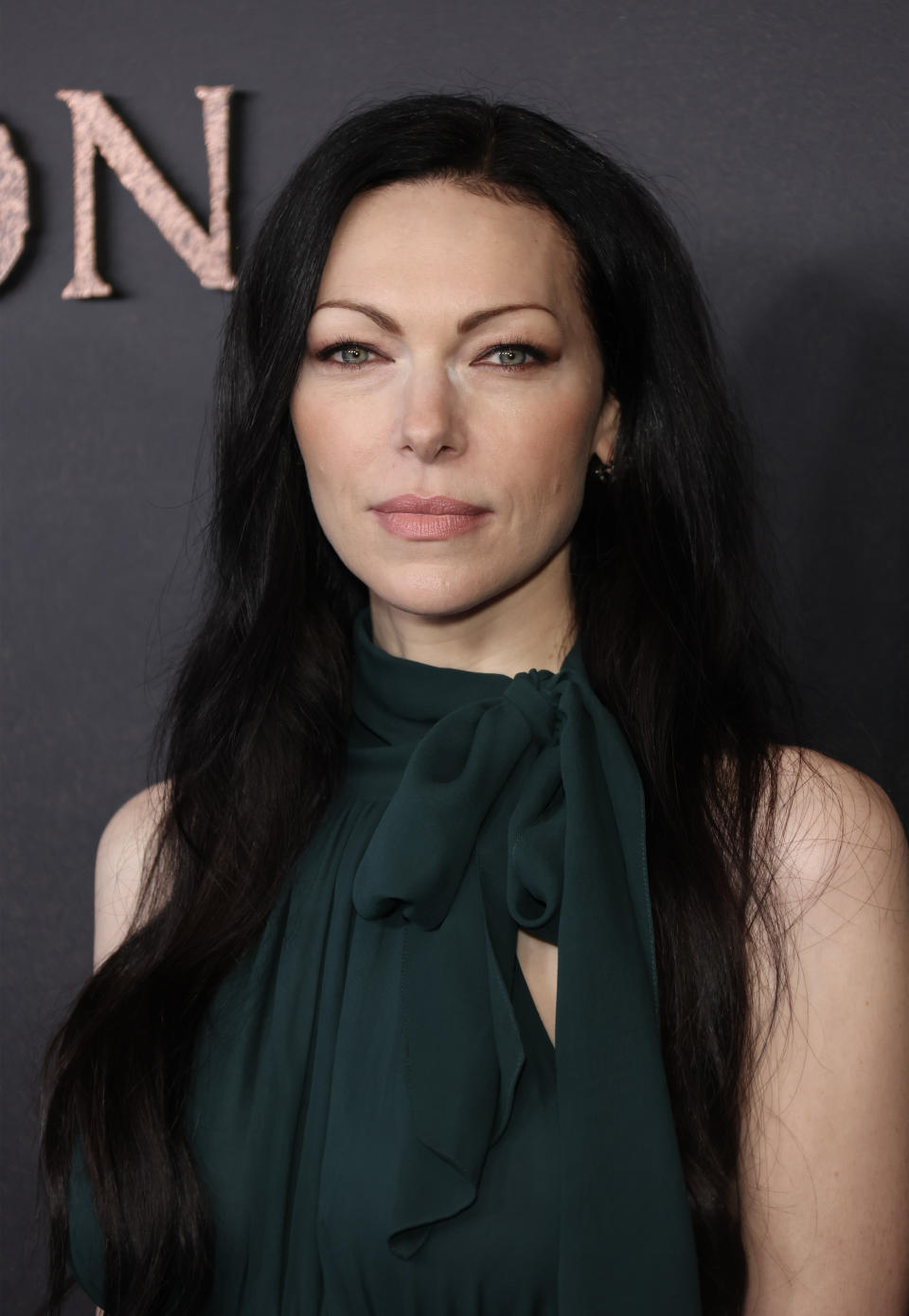 Laura Prepon at a red-carpet event, wearing a stylish, high-neck outfit with a bow detail