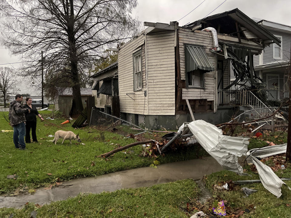 A man and a woman with a dog near a house that was damaged by a tornado.