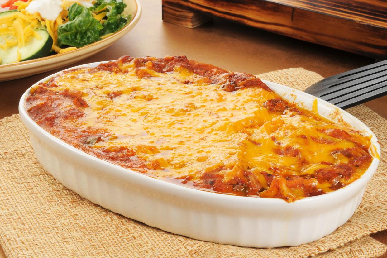 Chicken tortilla casserole in a white porcelain gratin dish on a natural napkin with a black spatula on a table next to a plate of salad