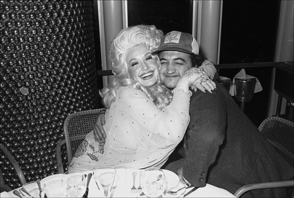 American Country musician Dolly Parton and comedian John Belushi (1949 - 1982) hug as they pose together at the Windows on the World restaurant (on the 107th floor of the World Trade Center), New York, New York, May 14, 1977. The event was an after party following Parton's performance at the Bottom Line. (Photo by Allan Tannenbaum/Getty Images)