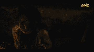 A scared young woman sits in a dark cavern