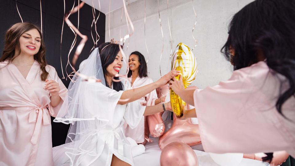 bride-to-be and her friends having fun and smiling while playing with the balloon decorations in the bedroom.