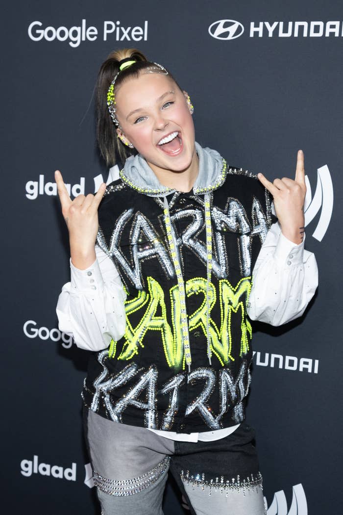 Person smiling and making peace signs, wearing jacket with "KARMA" text, at GLAAD event sponsored by Google Pixel and Hyundai