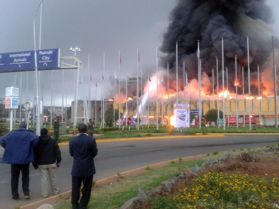 Onlookers watch as black smoke billows from the international arrival unit of Jomo Kenyatta International Airport in Nairobi, Kenya, Wednesday, Aug. 7, 2013. A massive fire engulfed the arrivals hall at Kenya's main international airport early Wednesday, forcing East Africa's largest airport to close and the rerouting of all inbound flights. (AP Photo/Segeni Ngethe)