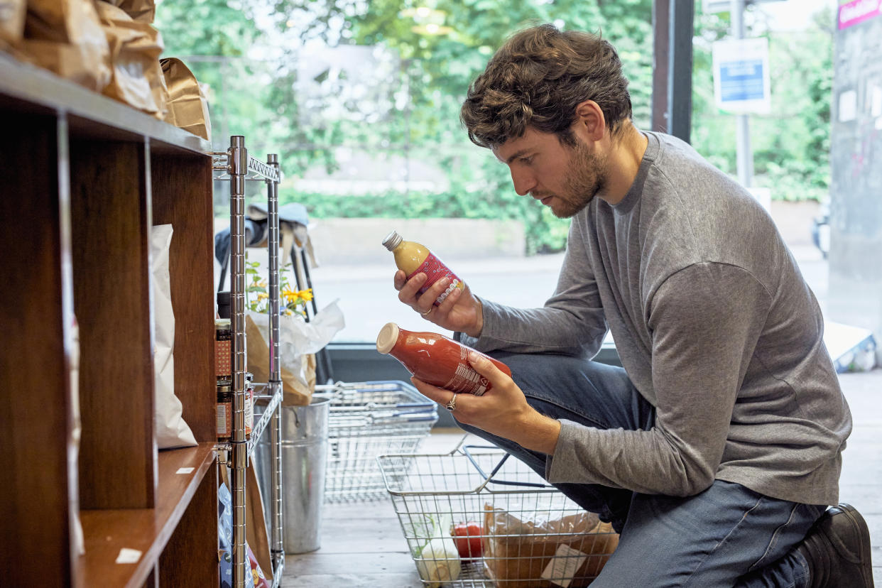 Young white man with beard in food store, he is holding two juice bottles.