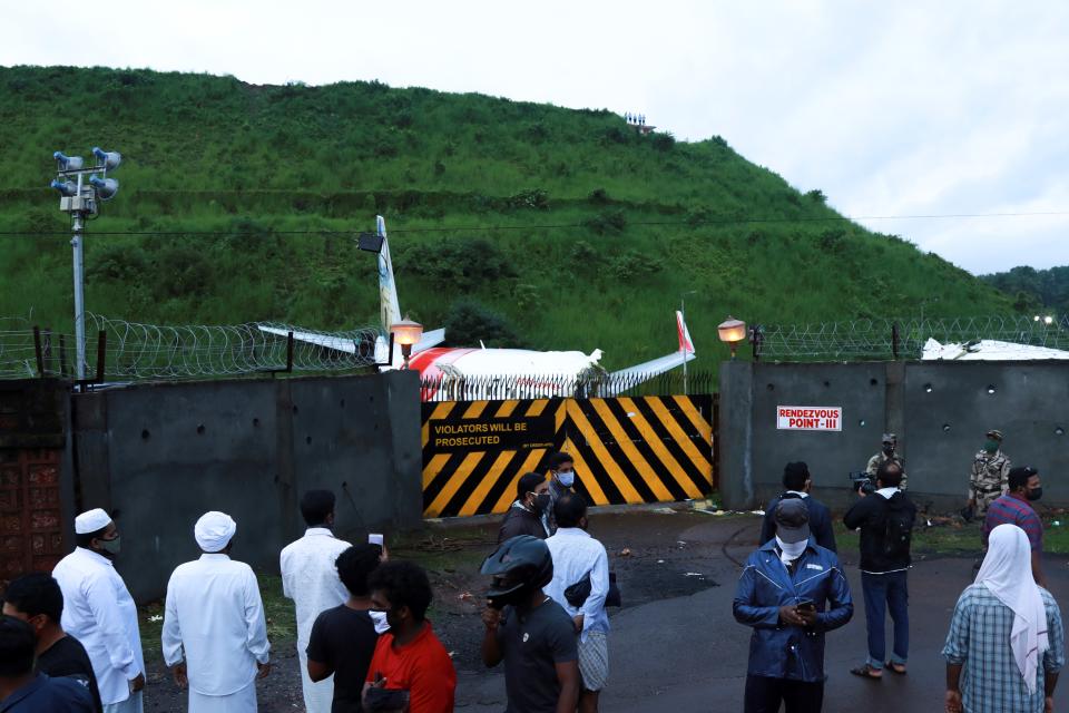 People gather outside a gate near the wreckage of an Air India Express jet at Calicut International Airport in Karipur, Kerala, on August 8, 2020. - Fierce rain and winds lashed a plane carrying 190 people before it crash-landed and tore in two at an airport in southern India, killing at least 18 people and injuring scores more, officials said on August 8. (Photo by Arunchandra BOSE / AFP) (Photo by ARUNCHANDRA BOSE/AFP via Getty Images)