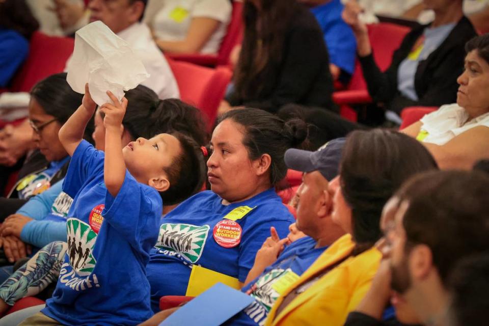 An unidentified child waves a white tissue as he sits on the lap of an agriculture worker while waiting for the Miami-Dade Commission to vote on the heat standard bill. Miami-Dade residents and stakeholders rallied in support or opposition to a potential array of protections for outdoor workers, a first in the nation county-level heat standard inside the Miami-Dade Commission chambers at County Hall in downtown Miami, Florida on Tuesday November 7, 2023. Carl Juste/Miami Herald