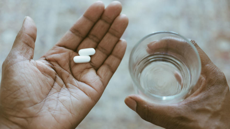 person with two capsules on their palm, holding a class of water in the other hand