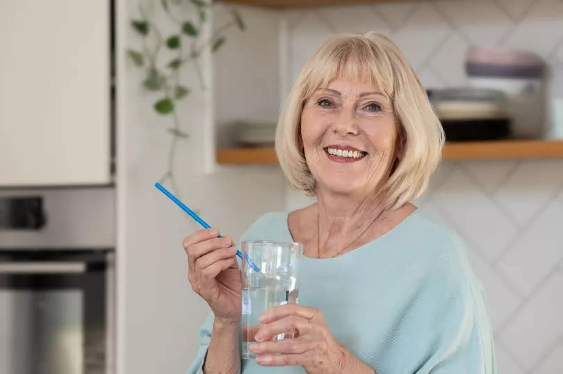 A mature woman drinks a cold drink with ice through a straw and feels severe pain in her teeth due to damage to the tooth enamel.