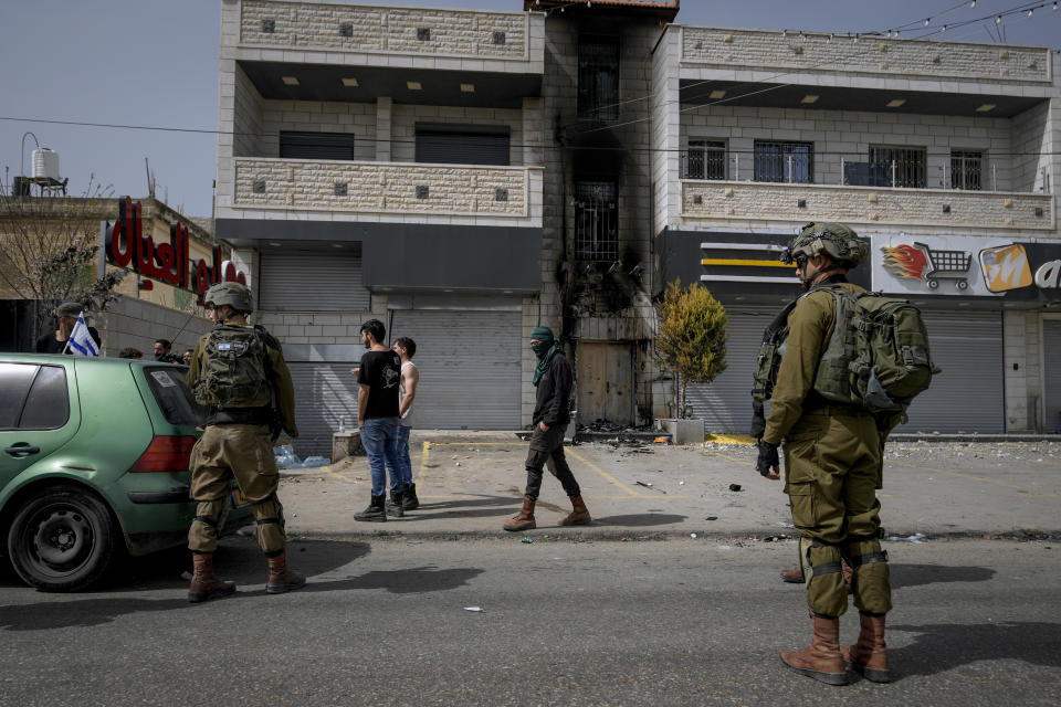 Israeli soldiers and Jewish settlers, some of them masked, stand next to a damaged Palestinian building in the town of Hawara, near the West Bank city of Nablus, Monday, Feb. 27, 2023. Scores of Israeli settlers went on a violent rampage in the northern West Bank, setting cars and homes on fire after two settlers were killed by a Palestinian gunman. Palestinian officials say one man was killed and four others were badly wounded. (AP Photo/Majdi Mohammed)