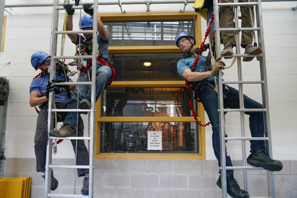 John Mansolillo, right, works with classmates to learn working-at-heights rescue techniques during a Global Wind Organisation certification class at the Massachusetts Maritime Academy in Bourne, Mass., Tuesday, Aug. 2, 2022. At the 131-year-old maritime academy along Buzzards Bay, people who will build the nation's first commercial-scale offshore wind farm are learning the skills to stay safe while working around turbines at sea. (AP Photo/Seth Wenig)