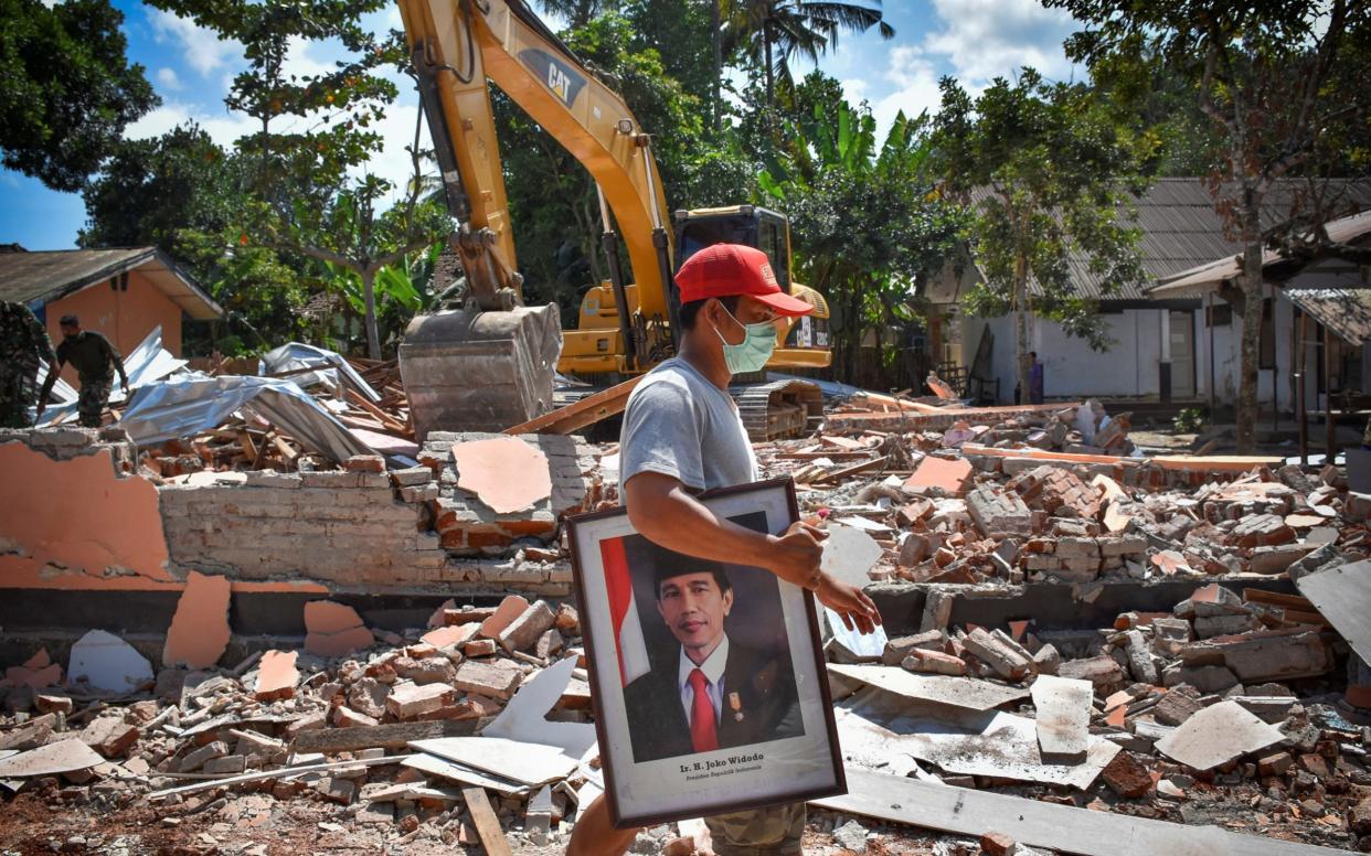 A man carries a framed picture of Indonesian President Joko Widodo from a school damaged by an earthquake in Gunungsari - REUTERS