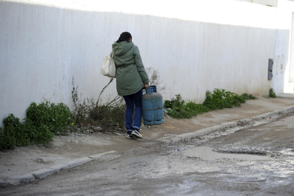 A woman carries gas canister in La Marsa, outside Tunis, Wednesday, Dec. 14, 2022. To outsiders, Tunisia’s legislative elections Saturday, Dec. 17, 2022 look questionable: Many opposition parties are boycotting. A new electoral law makes it harder for women to compete. Foreign media aren’t allowed to talk to candidates. But many voters believe that their country’s decade-old democratic revolution has failed, and welcome their increasingly autocratic president’s political reforms. (AP Photo/Hassene Dridi)