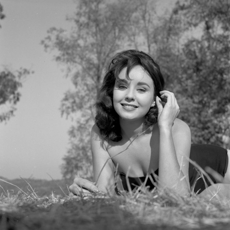 Miss USA 1956 Carol Morris lays in grass and smiles for a portrait.
