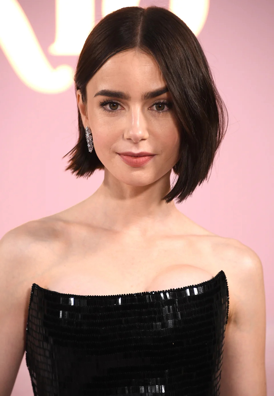 Lily Collins attends the "Emily in Paris" premiere in a sleek, black, strapless dress with sequins, short hairstyle, and statement earrings