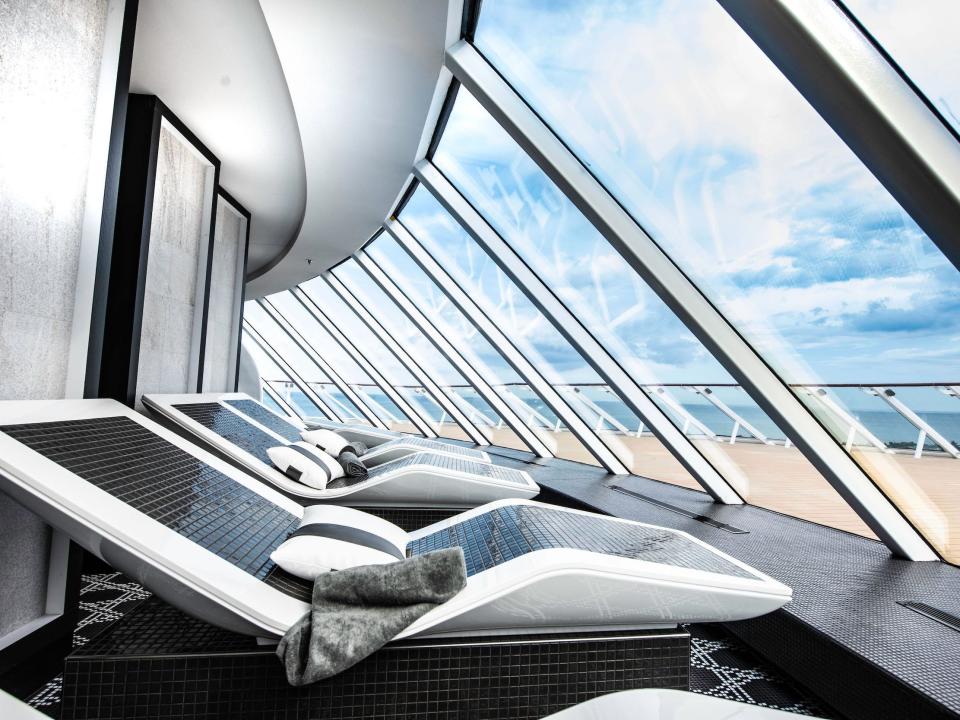 indoor black and white spa chairs overlooking a deck behind glass panels aboard the Celebrity Edge