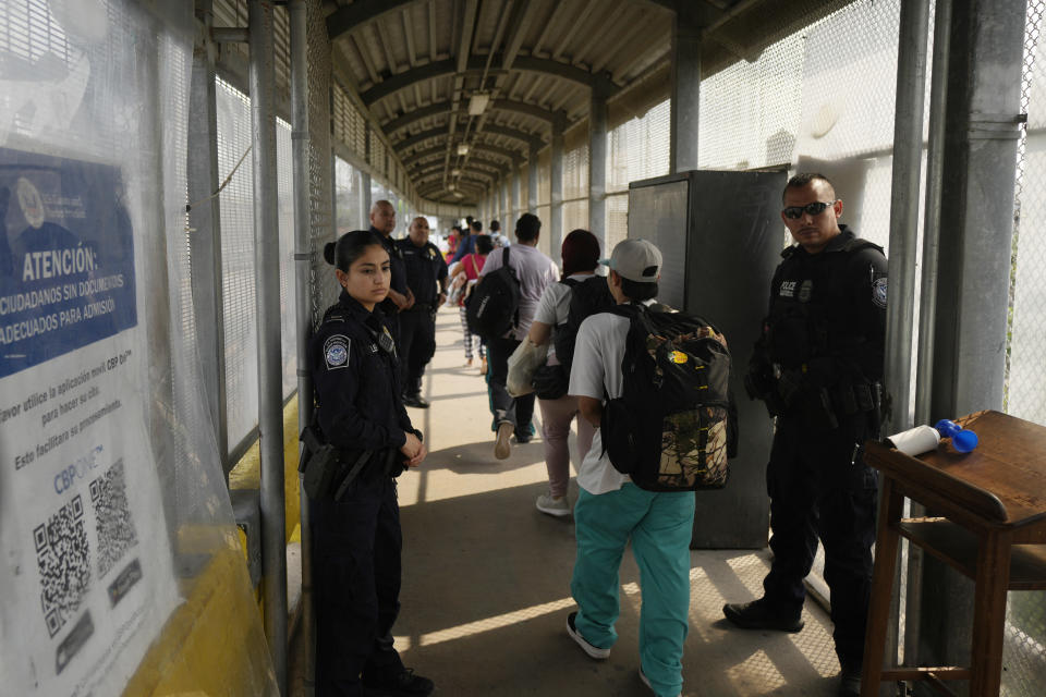 U.S. Customs and Border Protection Police monitor as migrants from a group of 50, who were chosen by the Mexican "Casa Migrante" organization, walk cross the Puerto Nuevo bridge from Matamoros, Mexico, to be processed by U.S. immigration officials, early Friday, May 12, 2023, the day after U.S. pandemic-related asylum restrictions called Title 42 were lifted. According to Mexican immigration officials, migrants will be organized to cross in groups of 50. (AP Photo/Fernando Llano)