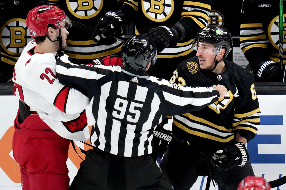 Boston Bruins left wing Brad Marchand, right, and Carolina Hurricanes defenseman Brett Pesce (22) are separated by linesman Jonny Murray (95) during the first period of an NHL hockey game Tuesday, April 9, 2024, in Boston. (AP Photo/Charles Krupa)