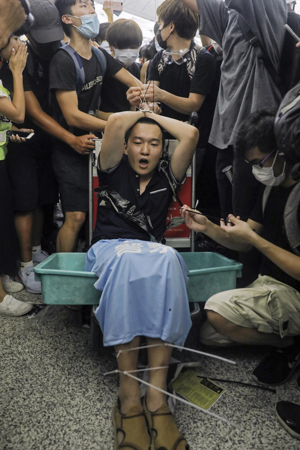 Protesters restrain a man on a luggage trolley, who protesters claimed was a Chinese undercover agent during a demonstration at the Airport in Hong Kong, Tuesday, Aug. 13, 2019. Riot police clashed with pro-democracy protesters at Hong Kong's airport late Tuesday night, a chaotic end to a second day of demonstrations that caused mass flight cancellations at the Chinese city's busy transport hub. (AP Photo/Vincent Yu)