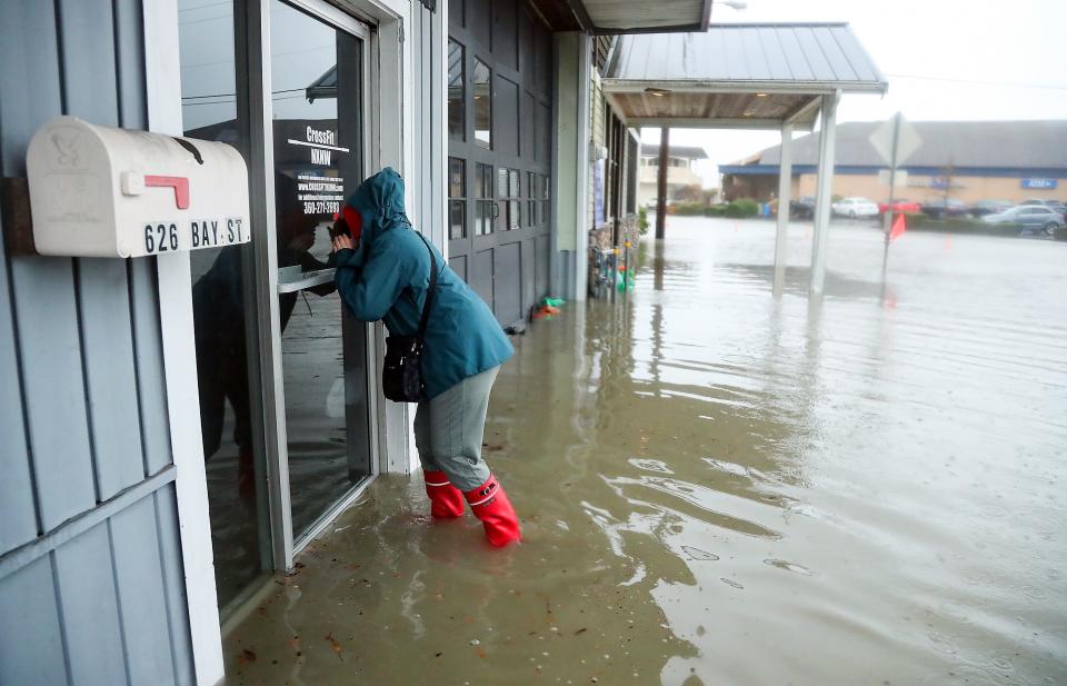 CrossFit NXNW owner Maureen Pace peers into the windows to see the flood damage inside the space that they just moved their business out of on Monday, on Bay Street in downtown Port Orchard on Tuesday, Dec. 27, 2022. CrossFit NXNW is now located in the West Bay Center complex.