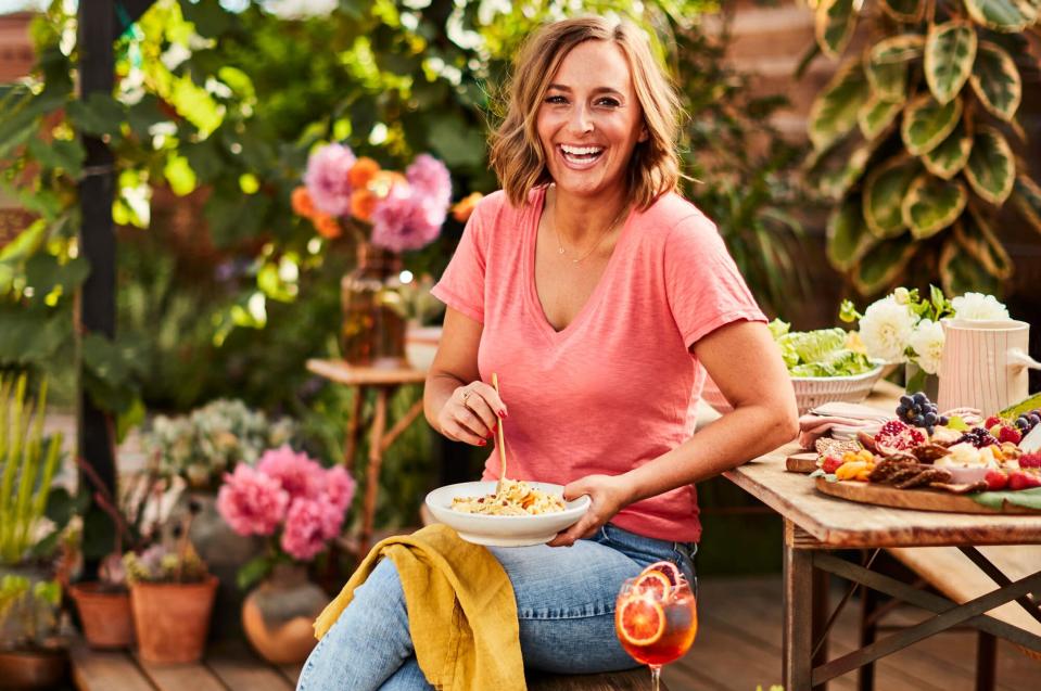 Women in jeans and pink top seated outside with bowl of pasta