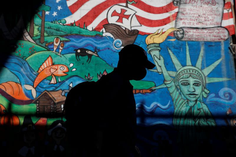 A man in silhouette wearing a protective face mask walks past a mural, amid the coronavirus disease (COVID-19) pandemic, in the Queens borough of New York