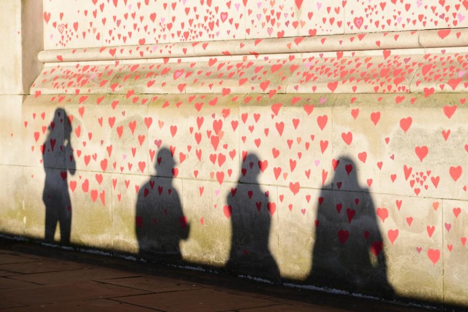 People are silhouetted against the Covid-19 Memorial Wall on the Embankment, central London (Ian West/PA) (PA Wire)