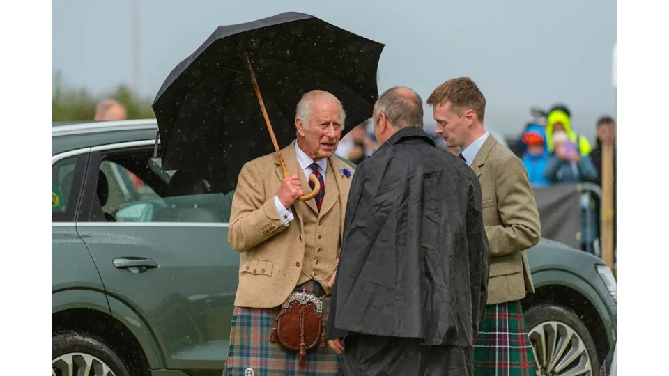 King Charles in a kilt holding a black umbrella