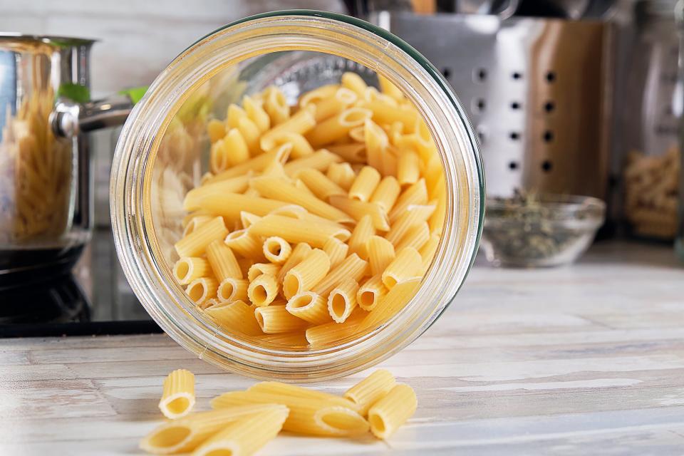 Dried penne pasta spills out of a jar