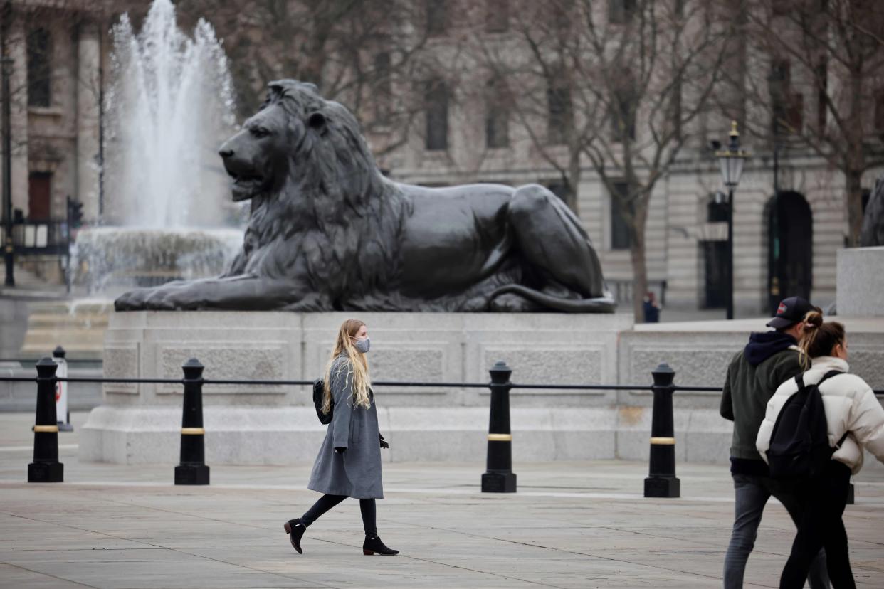 A wears a facemask as she crosses a near-deserted Trafalgar Square in central London (AFP via Getty Images)
